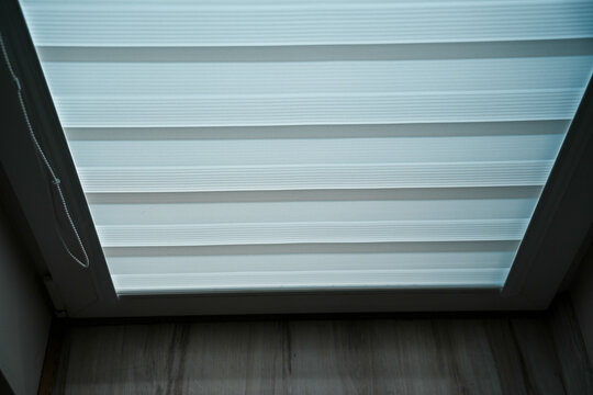 Zebra blind covering a window in a dark room with wooden floor visible below, concept of window treatment and home interior