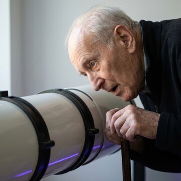 Elderly astronomer studying a telescope in soft indoor light