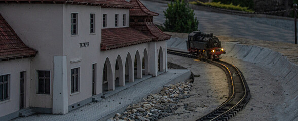 Miniature model of a railway station building and a steam locomotive on curved tracks at dusk © ArtExpert
