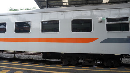 Sleek train carriage exterior with orange stripe design, parked at station platform under covered roof shelter. © anungcamui