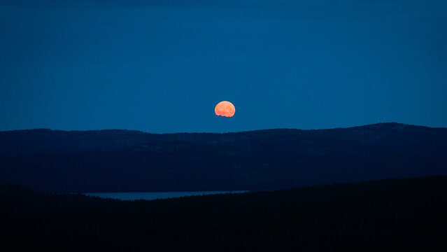 Sandoverken, Sweden - 08 August 2025: Aerial view of a full moon rising over the dark forested hills and landscape at twilight.