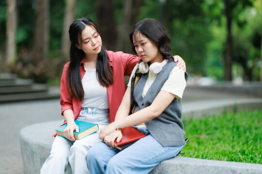 Young Asian female student comforting sad friend outdoors, showing empathy and support during a difficult time, highlighting concepts of friendship and care