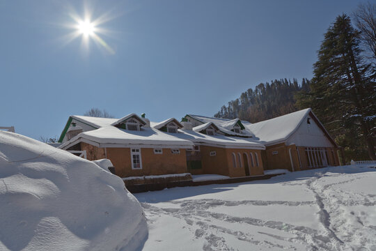 View of a snow-covered house with dormer windows under a bright sun and clear blue sky in the Galiyat region, Nathia Gali, Khyber Pakhtunkhwa, Pakistan.