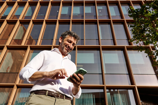 Smiling businessman uses smartphone outdoors in Barcelona