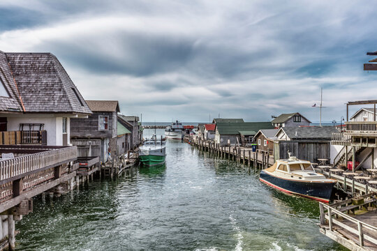 Leland, United States - 24 April 2017: Aerial view of Historic Fishtown with its iconic weathered shanties, fishing boats docked along the narrow channel, and a dramatic cloudy sky over Lake Michigan.