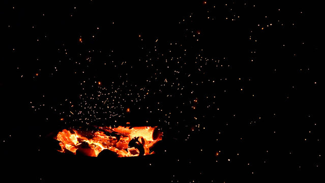 Glowing fire sparks and glowing embers flying against a dark black background. Abstract fiery texture for compositing, screen mode overlays, and dramatic design backgrounds.