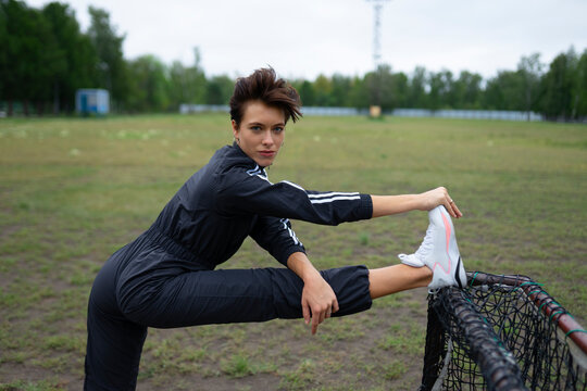 Athletic woman stretches her leg on a net in a grassy field