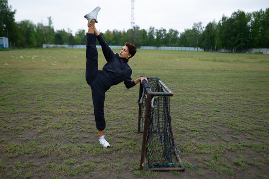 Athletic woman stretches her leg on a soccer goal outdoors