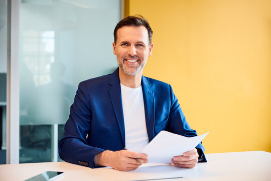 Smiling businessman holding document at office desk