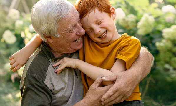 A grandfather and grandson are hugging and laughing in the garden