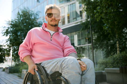 Confident man in pink sweatshirt sits in wheelchair in the city