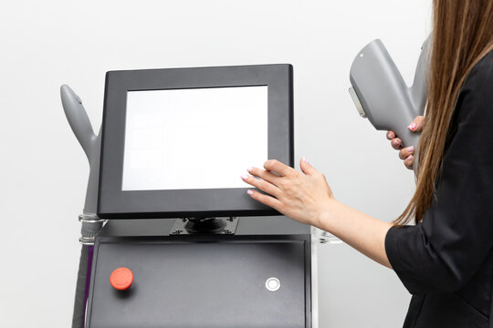 Cropped woman interacts with modern aesthetic treatment device with touchscreen display and handheld applicators for effective body treatment and skin care on white background in modern beauty clinic