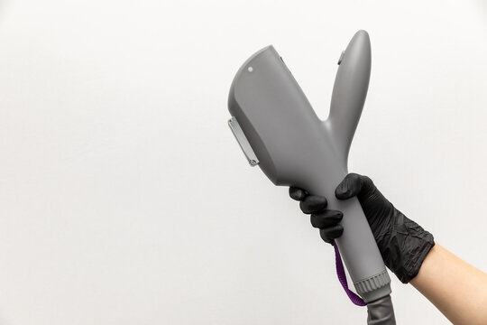 Hand wearing a black glove holds a gray laser hair removal device on white background. Modern and advanced beauty technology. Working part of epilator in the woman hand