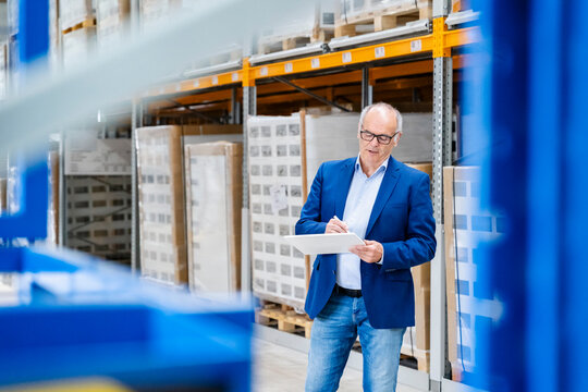 A businessman checks inventory on a tablet in a warehouse