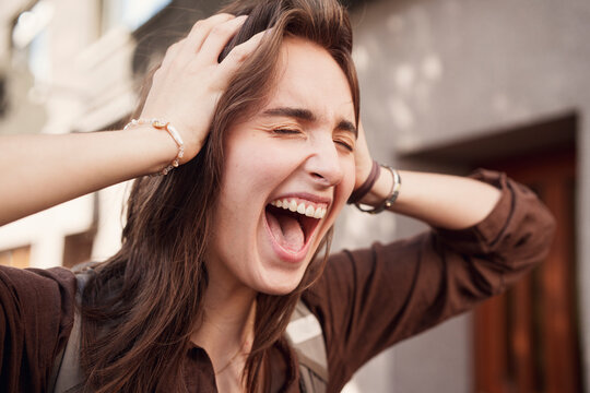 A happy woman holds her head and laughs outdoors