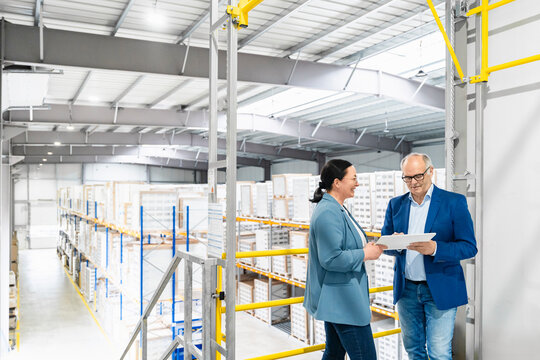 Mature woman and senior man discussing logistics with tablet in warehouse