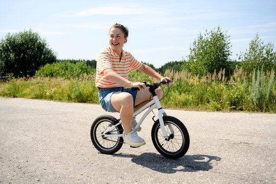 Happy woman rides a small toy bicycle on a road outdoors in summer