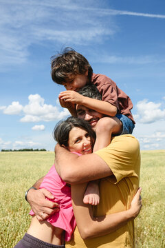 Happy mother and father hug their boy in a sunny summer field