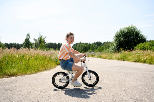 Woman rides a small bike on a rural road in summer