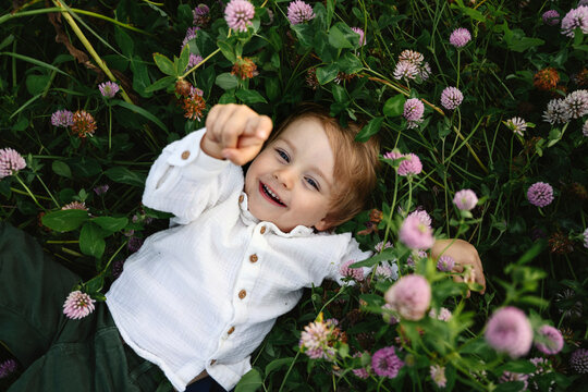 Smiling boy points at camera while lying in a green meadow