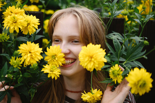 A smiling girl holds a yellow flower in the summer garden
