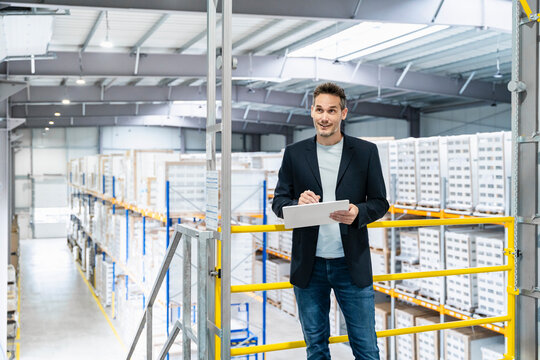 Male manager checks inventory on tablet in large warehouse