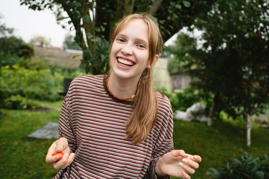 A smiling girl holds a fresh tomato in the summer garden