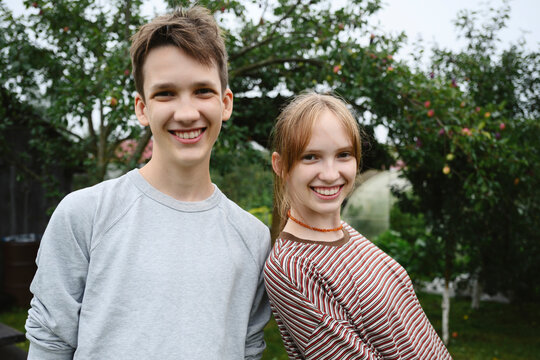 A teenage boy and girl smile together in a summer garden