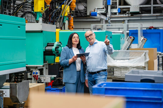 A businessman and a businesswoman discuss production in a factory