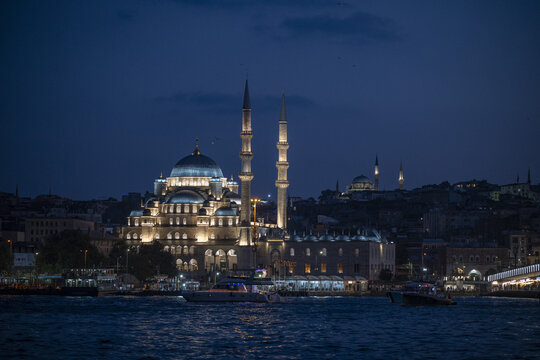View of the illuminated New Mosque at night with boats on the Bosphorus in Istanbul, Istanbul, Turkiye.