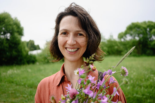 A smiling woman holds a bouquet of wildflowers outdoors in summer