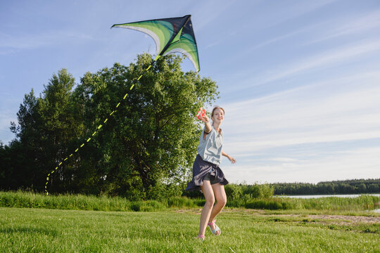 Happy girl flies a green kite in a sunny summer park