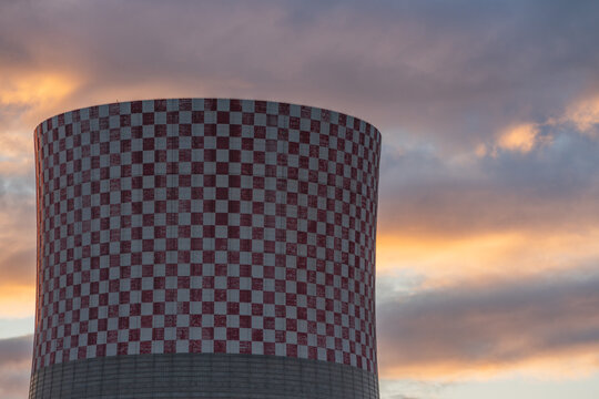 View of the red and white checkered cooling tower of the Jaworzno Power Station against a dramatic sunset sky in Jaworzno, Silesian Voivodeship, Poland.