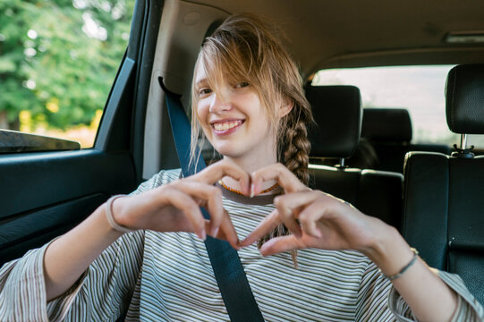 Smiling girl making heart symbol in the back seat of a car
