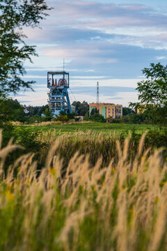 View of the historic mine headframe rising above a field of tall grass with residential buildings in the background in Jaworzno, Silesian Voivodeship, Poland.