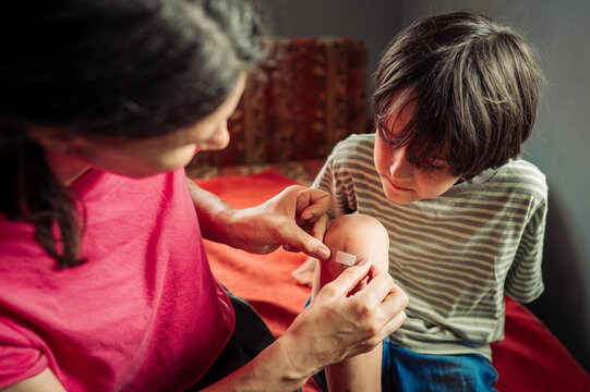 Mother applies a bandage to her son's wounded knee indoors