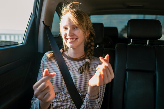 A smiling girl in a car makes a heart symbol with her fingers