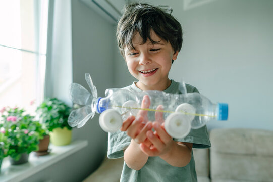 Smiling boy holds a toy car made from a recycled plastic bottle