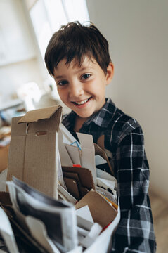 Cheerful boy holds paper waste for recycling at home