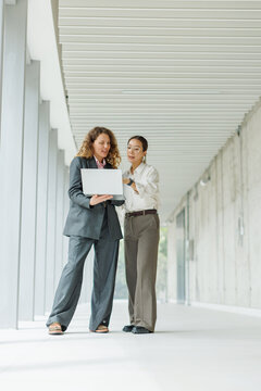 Businesswoman shows laptop to colleague in the office corridor