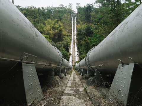 View of the massive steel inverted siphon pipelines of Talangagung Metro Syphon transporting irrigation water across a lush valley in Malang, East Java, Indonesia.