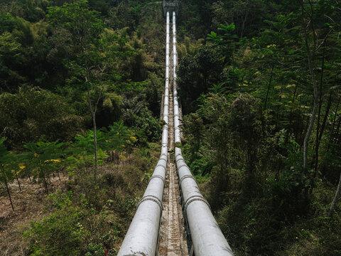 View of the massive steel inverted siphon pipelines of Talangagung Metro Syphon transporting irrigation water across a lush valley in Malang, East Java, Indonesia.