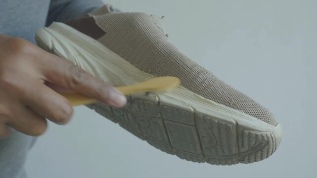 Close up video of person holding brown sports shoe and using a small wooden brush to clean off dirt and grime from the sole, demonstrating meticulous shoe care and maintenance
