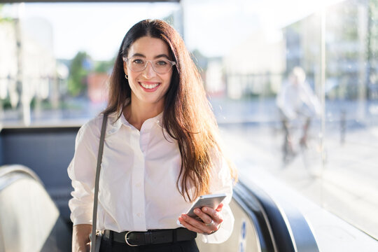 Smiling businesswoman holds a smartphone on a subway escalator