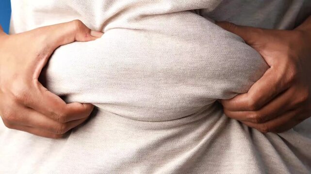 Close-up shot of a person pinching their belly fat demonstrating weight gain, unhealthy lifestyle, and the need for diet or exercise footage