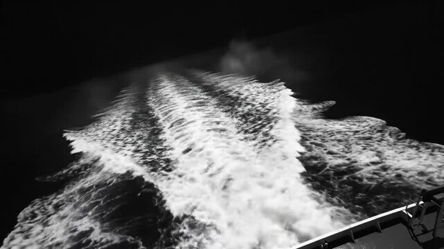 Black and white view of a ship's wake in ocean water on a dark, mysterious night