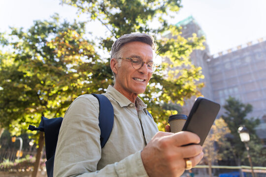 Smiling man checks smartphone holding coffee in Barcelona park