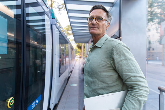Man holding laptop waits for tram at station in Barcelona Spain