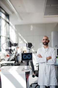 Male scientist stands next to a robotic arm in a bright laboratory