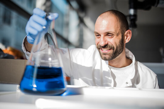 Smiling scientist analyzes blue liquid in the laboratory
